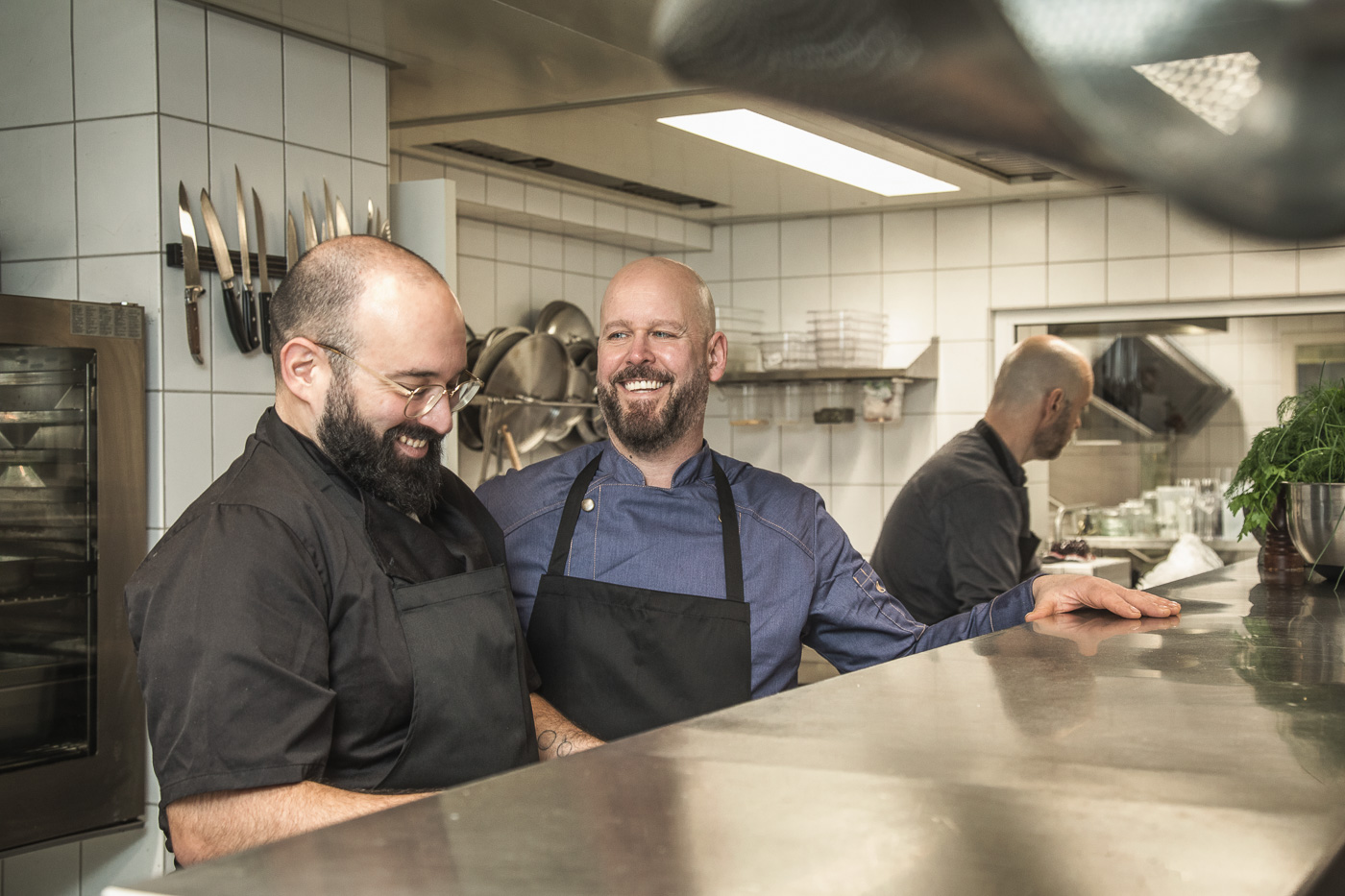 Dokumentarische Fotografie in der Küche beim Catering-Unternehmen. Man sieht den Chef im freundlichen Austausch mit seinem Mitarbeiter.