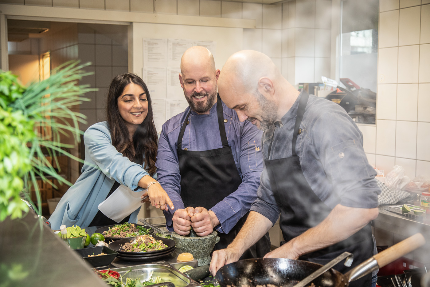 Dokumentarisches Teamfoto in Aktion in der Küche beim Catering-Unternehmen. Man sieht den Chef in Aktion mit seinen Mitarbeitern.