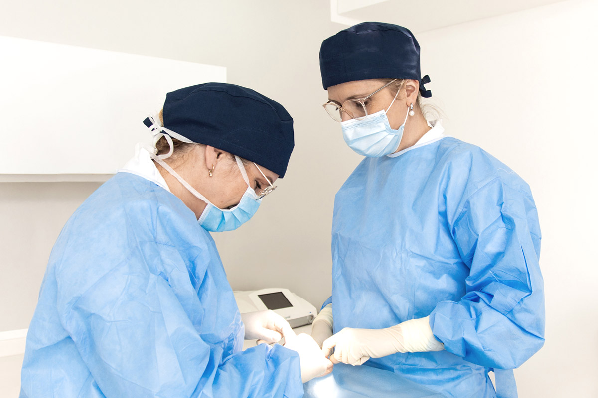 Ärzte tragen blaue OP-Kittel, OP-Hauben und Mundschutz, während sie am Patienten operieren.